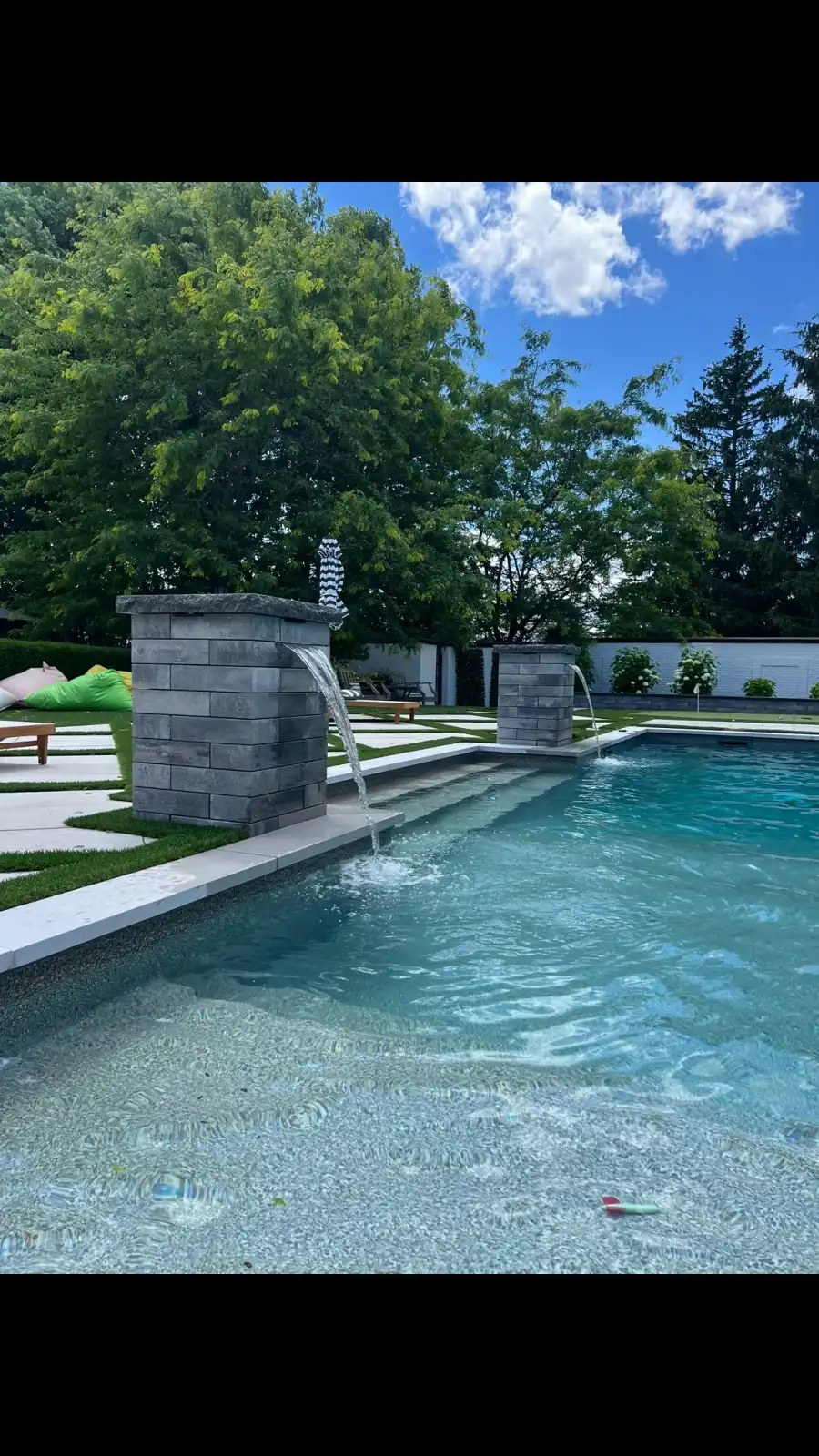 Long pool with water fountains and a wide stone patio