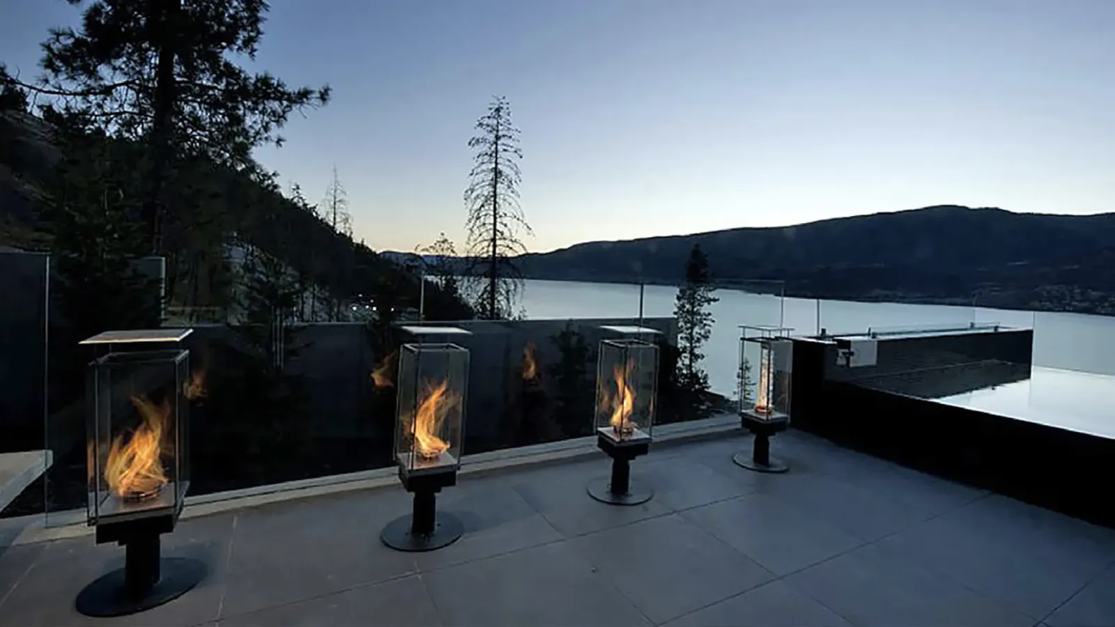 Fire bowls burning on a lakeside patio at sunset